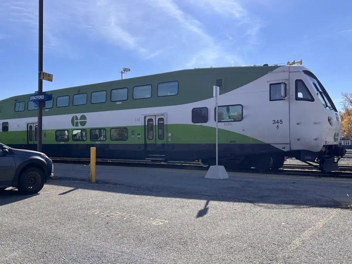 A green and white GO train at the Stratford platform on a sunny day