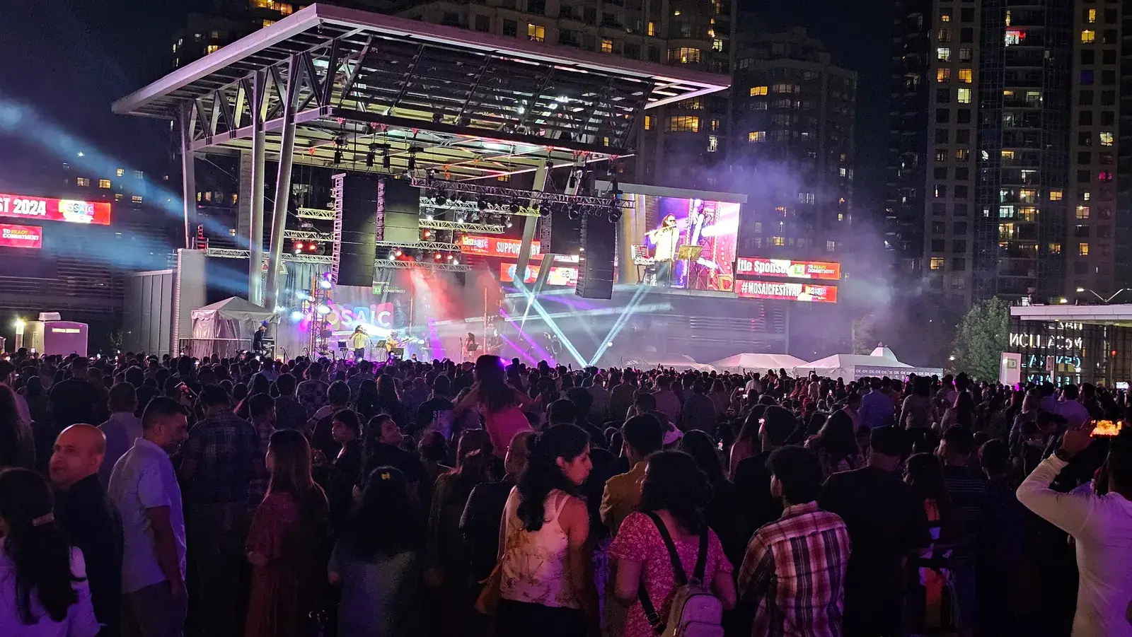 Thousands of people in front of the lit-up main stage at Celebration Square at night